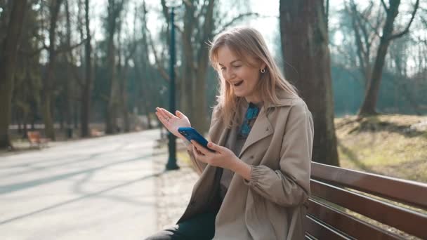 Счастливая Улыбающаяся Молодая Блондинка Сидящая Улице Зеленом Парке Мобильным Телефоном — стоковое видео