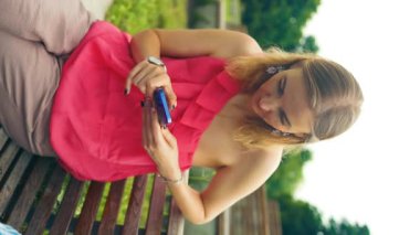 Çekici 30 'lu yaşlardaki sarışın kadın şehir merkezinde telefon yürüyüşü yapıyor dışarıda bir bankta oturuyor, teknolojili göz kapağı aracı. Yüksek kaliteli FullHD görüntüler