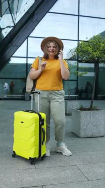 30 'lu yaşlarda şık giyinmiş ve şapka takan mutlu bir beyaz kadın cep telefonu kullanıyor. İnternet' ten seyahat yerini kontrol ediyor. Uçuş kapısında bekleyen kadın uçağa binmek ve gülümsemek için bekliyor.