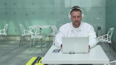 Mutlu 30 'lu yaşlardaki beyaz adam havaalanı terminalinde oturup bilgisayarla video aracılığıyla konuşuyor. Erkek uçuş, internet, sosyal medya, online alışveriş bekliyor. 