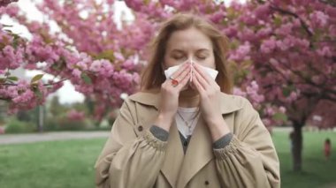 Sağlık sorunları. Baharda çiçek açan sakura ağacı poleni yüzünden alerji belirtileri gösteren güzel sarışın bir kadın. Dışarıda hapşırma polen alerjisi olan bir kadın.