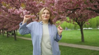 Şehirde çevrimiçi müzik dinleyen mutlu beyaz kadın portresi. Baharda mavi gökyüzünde güzel kiraz çiçekli sakura. Japon sakurası. Yüksek kaliteli FullHD görüntüler