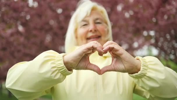 Uśmiechnięta Biała Blondynka Seniorka Dwiema Rękami Znak Miłości Piękny Kwiat — Wideo stockowe