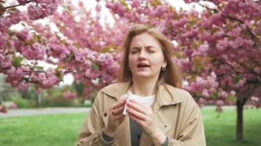 Sağlık sorunları. Baharda çiçek açan sakura ağacı poleni yüzünden alerji belirtileri gösteren güzel sarışın bir kadın. Dışarıda hapşırma polen alerjisi olan bir kadın.
