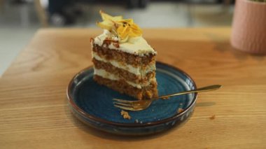 Kadın bir parça kahveli kek veriyor. Kafede çatal kesimli çikolatalı kek ve kremalı meyve süslemesi kullanan kadını kapat. Mavi tabakta dilimlenmiş kek. Tahta masada servis edilmiş. En Sevilen