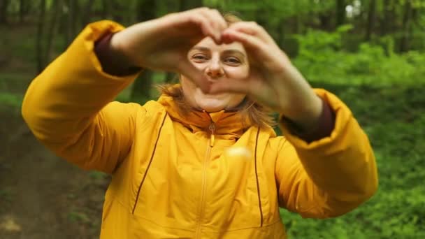 女性的手手用手指做记号心 年轻的高加索女人在大自然中徒步旅行和露营 背着背包在森林里散步的人 慈善的象征 — 图库视频影像