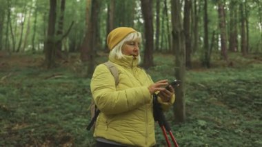 60 'lı yaşlarda akıllı telefonlu, elinde haritayla bir dağın tepesinden manzarayı seyreden kayıp bir kadının fotoğrafı. Dişi turist dağdaki kayada oturuyor ve haritayı okuyor. Polonya, Tatry 
