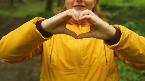 女性的手手用手指做记号心 年轻的高加索女人在大自然中徒步旅行和露营 背着背包在森林里散步的人 慈善的象征 — 图库视频影像