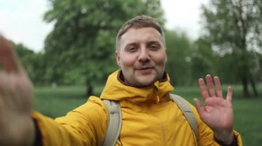 Gezgin, sakallı beyaz adam cep telefonu kullanarak doğa parkında duruyor. Yeşil orman arka planında selfie ya da video görüşmesi yapan gülümseyen genç erkek turistin portresi. 
