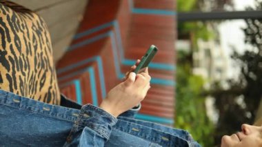 30 'lu yaşlardaki şık giyinen mutlu sarışın kadın Central City caddesinde bir bankta oturuyor ve telefonunu kullanıyor.. 