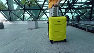 Havaalanının geçiş bölgesindeki bir kadın bir sonraki uçağa atlamak ve başka bir ülkeye gitmek için acele ediyor. Parlak sarı pantolonlu kadın bacaklarının yakın görüntüsü. Bir kadın tekerlekli bavulu sürüklüyor.