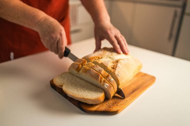 Tam tahıllı ekmek mutfak ahşap tabağına konmuş ve şefin elinde altın bıçak var. Masanın üzerinde taze ekmek var. Mutfak masasında taze ekmek sağlıklı beslenme ve geleneksel fırın konsepti