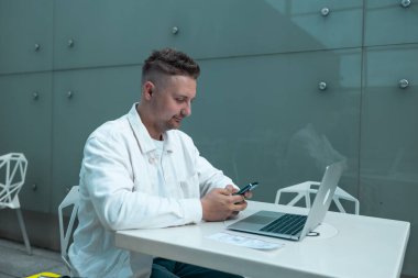 Akıllı telefon ve dizüstü bilgisayar kullanarak şık giyinen beyaz erkek yolcu, havaalanındaki dizüstü bilgisayarında eğitim toplantısı yapıyor. Uluslararası havaalanı transit havaalanı..