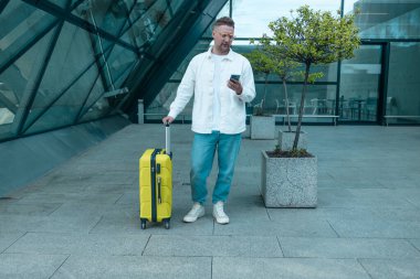 Akıllı telefon ve dizüstü bilgisayar kullanarak şık giyinen beyaz erkek yolcu, havaalanındaki dizüstü bilgisayarında eğitim toplantısı yapıyor. Uluslararası havaalanı transit havaalanı..