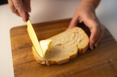 Genç kadın elleri ekmeğe tereyağı sürüyor, yakın çekim.