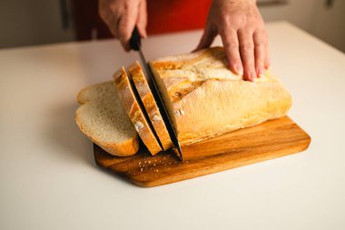 Tam tahıllı ekmek mutfak ahşap tabağına konmuş ve şefin elinde altın bıçak var. Masanın üzerinde taze ekmek var. Mutfak masasında taze ekmek sağlıklı beslenme ve geleneksel fırın konsepti