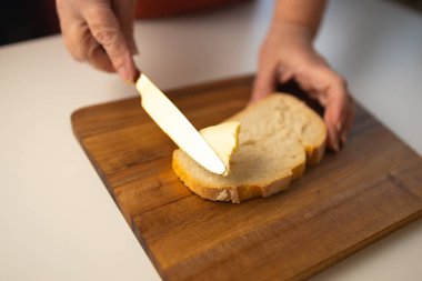 Genç kadın elleri ekmeğe tereyağı sürüyor, yakın çekim.