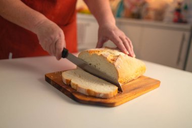 Tam tahıllı ekmek mutfak ahşap tabağına konmuş ve şefin elinde altın bıçak var. Masanın üzerinde taze ekmek var. Mutfak masasında taze ekmek sağlıklı beslenme ve geleneksel fırın konsepti