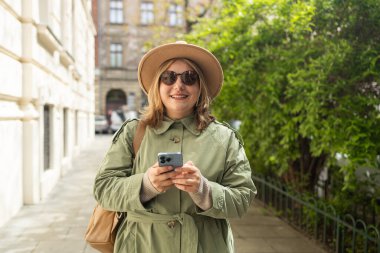 Açık havada yürürken cep telefonu kullanan neşeli, beyaz, sarışın bir kadının portresi. Şık sarışın, başka tarafa bakıyor ve şehirde gülümsüyor.. 