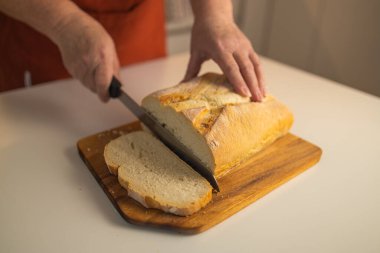 Tam tahıllı ekmek mutfak ahşap tabağına konmuş ve şefin elinde altın bıçak var. Masanın üzerinde taze ekmek var. Mutfak masasında taze ekmek sağlıklı beslenme ve geleneksel fırın konsepti
