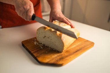 Tam tahıllı ekmek mutfak ahşap tabağına konmuş ve şefin elinde altın bıçak var. Masanın üzerinde taze ekmek var. Mutfak masasında taze ekmek sağlıklı beslenme ve geleneksel fırın konsepti