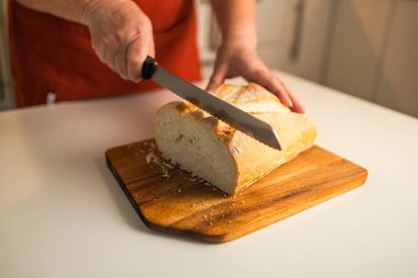 Tam tahıllı ekmek mutfak ahşap tabağına konmuş ve şefin elinde altın bıçak var. Masanın üzerinde taze ekmek var. Mutfak masasında taze ekmek sağlıklı beslenme ve geleneksel fırın konsepti