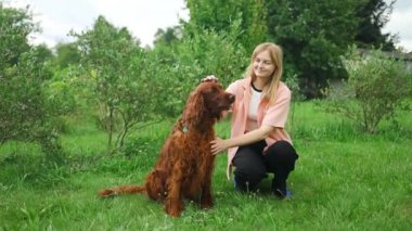 Beyaz bir kadın, İrlandalı bir Setter köpeğiyle oynayarak eğleniyor, akşamları kır evinin arka bahçesindeki yeşil çimlerde oturuyor. Yaşam tarzı ve arkadaşlık kavramları. Yüksek kalite FullHD