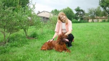 Beyaz bir kadın, İrlandalı bir Setter köpeğiyle oynayarak eğleniyor, akşamları kır evinin arka bahçesindeki yeşil çimlerde oturuyor. Yaşam tarzı ve arkadaşlık kavramları. Yüksek kalite FullHD