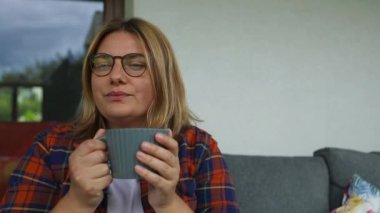 Arka bahçede kanepede oturup kahve ya da çay içen hayalperest genç bayanı yakından çek. Rahat sahne Yüksek kalite FullHD görüntüler