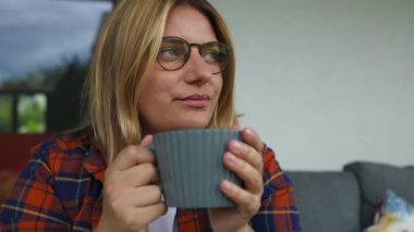 Arka bahçede kanepede oturup kahve ya da çay içen hayalperest genç bayanı yakından çek. Rahat sahne Yüksek kalite FullHD görüntüler