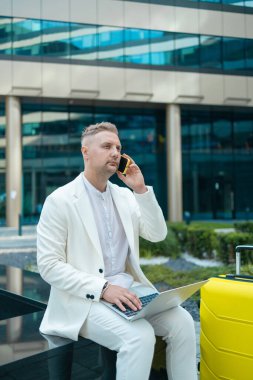 Yakışıklı genç bir iş adamının portresi çantasıyla seyahat ediyor ve dışarıda bir iş merkezinin yakınında telefonla konuşuyor. Yüksek kalite fotoğraf