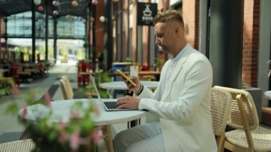 Uzaktan kumandayla çalışan mutlu Avrupalı işadamı dışarıda, şehir merkezindeki kafede oturup konuşuyor ve gülümsüyor. Yüksek kaliteli FullHD görüntüler