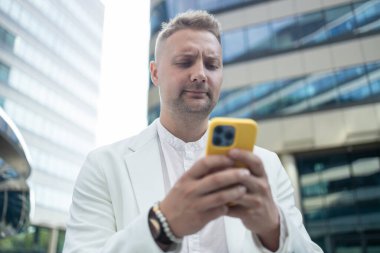 Bir iş merkezinin yakınında yürüyen ve cep telefonu kullanan kızgın bir şirket yatırımcısı. Yüksek kalite 