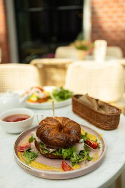 Sebzeli taze kruvasan sandviçler, tohum ve un dolu bir masada et ve peynir. Arka planda bir fincan aromatik çay. Yüksek kalite 