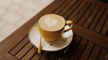 Doğal sanatı olan sarı latte kahve fincanı. Kahve fincanındaki sütlü sütlü sütlü sütlü sütlü sıcak kahve kafedeki bir kahve masasında. Yüksek kaliteli FullHD görüntüler