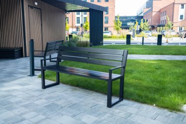 Yeşil çimenli asfalt yol, dekoratif çimenler ve modern ahşap bankların önünde kablodan yapılmış ve modern ofis binasının yakınlarındaki dinlenme alanında taşlarla doldurulmuş gabion ağaç küvetlerinin manzarası.