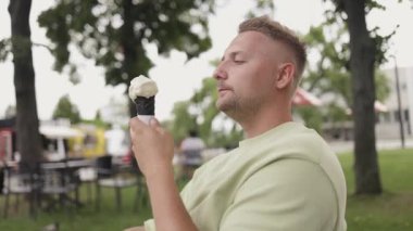 Şehir parkında dondurma yerken mutlu bir şekilde gülümseyen 30 'lu yaşlardaki beyaz bir genç. Yüksek kaliteli FullHD görüntüler