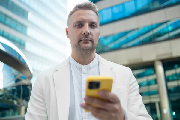 stock image Focused young corporate worker investor businessman walking and using mobile phone outdoors near a business centre. High quality 