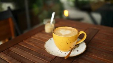 Doğal sanatı olan sarı latte kahve fincanı. Kahve fincanındaki sütlü sütlü sütlü sütlü sütlü sıcak kahve kafedeki bir kahve masasında. Yüksek kaliteli FullHD görüntüler. Yüksek kaliteli FullHD görüntüler