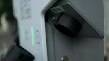 Kafkasyalı bir kadının elektrikli bir arabayı açarken, soket kapağını açarken ve şarj aletini takarken yakın çekim. Şarj istasyonunda elektrikli arabalar şarj oluyor.. 