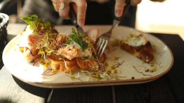 Kadının orta seçim somon tostu kesmek için çatal ve bıçak kullanır. Restoranda kahvaltı.. 