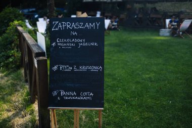 Polonya, Ağustos - 2024: Yaz parkındaki şehir kafesinde kara tahta menülü açık hava kafe sahnesi. Reklam işi konsepti için kaldırımda duran yeşil metal çerçeveli boş bir karatahta. Yüksek
