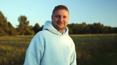 Yakışıklı adam gün batımında genç yeşil bir tarlada yürüyor. Forest Park 'ta gün batımında kameraya gülümseyen bir erkek. Yüksek kaliteli FullHD görüntüler