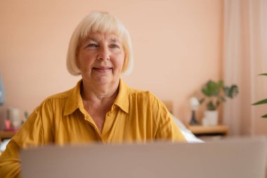 Evde dizüstü bilgisayarla çalışırken kameraya bakan mutlu bir son sınıf kadını. Güzel, şık, yaşlı bir kadın cep telefonunda geziniyor. Yüksek kalite fotoğraf