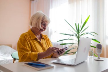 Evde dizüstü bilgisayar kullanan yaşlı bir kadın. Not defteri ve kalemle bilgisayar başında gözlük takan kıdemli stil girişimcisi. Ev faturalarını ve ev finansmanını inceleyen ve yöneten ciddi bir kadın.