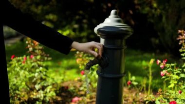 Şehrin sokaklarında ya da parklarında içme suyuyla musluğu açıp kapatan bir kadın eli. Akan su. Seçici odak