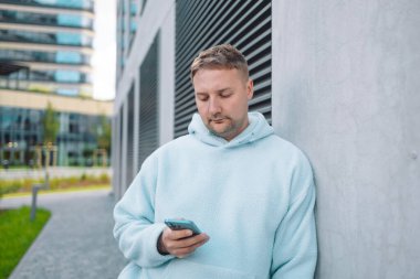 Güler yüzlü iş adamı şehir merkezinde telefonla dışarıda dolaşıyor. İş ortamında modern yaşam tarzı, iletişim ve teknolojiyi yansıtan kendine güvenen erkek akıllı telefon.