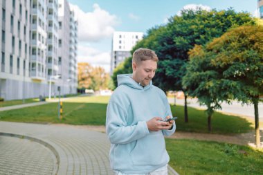 Genç beyaz adam, şehir parkında sesli mesaj göndermek için cep telefonu uygulamasını kullanıyor.