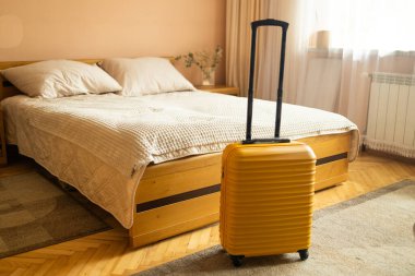 Yatağın yanında sarı valizli otel odasının içi. Otelden otele giriş yaptıktan sonra. Seyahat ve tatil kavramı. Yüksek kalite fotoğraf