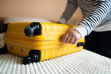 Beyaz kadın elbiselerini sarı bavula koyup tatil gezisi için çantalarını kilitlemeye çalışıyor, yaz yolculuğuna hazırlanıyor. Seyahat kavramı